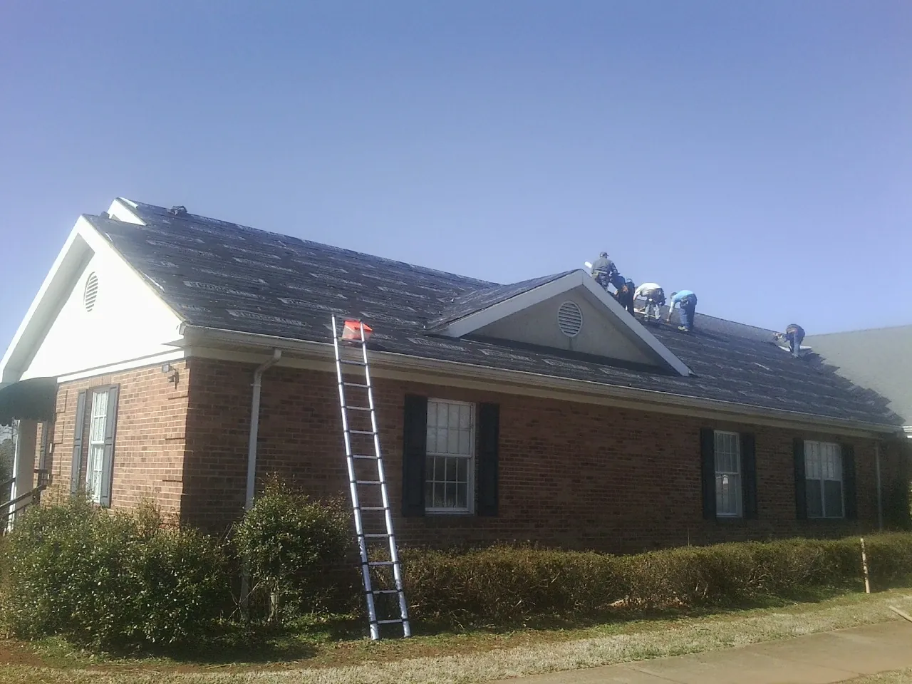Crew tearing shingles off a brick ranch roof with a ladder set — Emergency Roof Repair work by our crew in Elgin