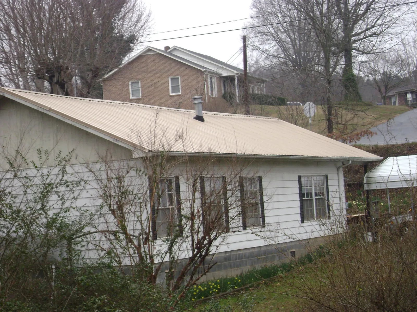 Tan metal roof on a white sided house set into a hillside — Commercial Roofing by Roofing Brothers in Elgin